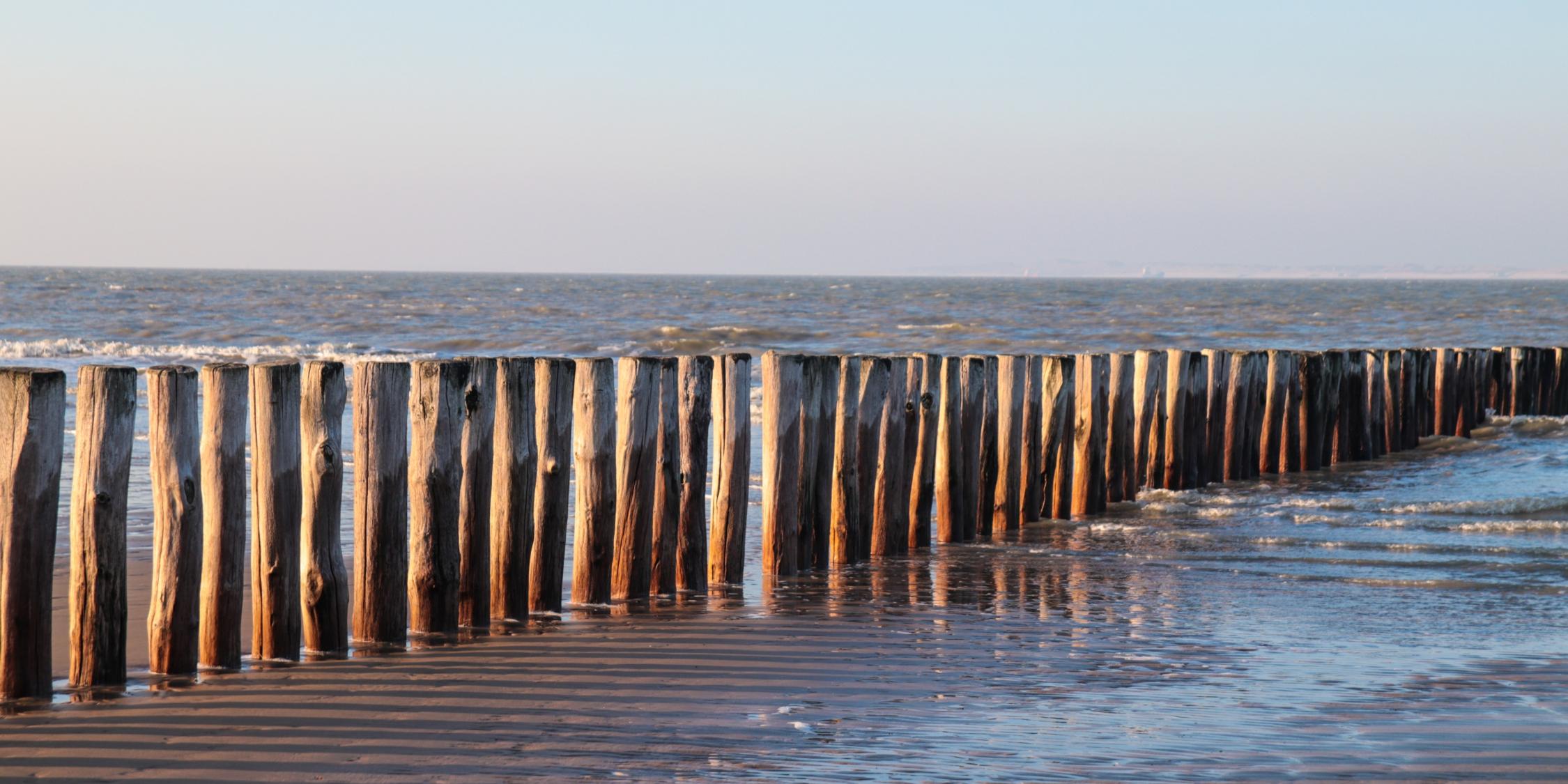 Blick vom Strand auf das Meer über eine Reihe Strandpfähle hinweg