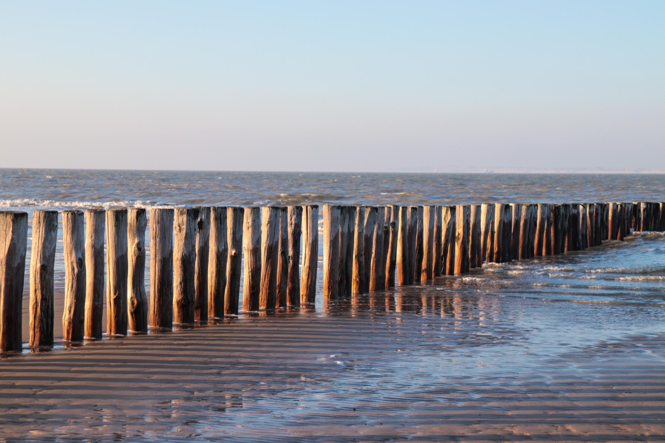 Blick vom Strand auf das Meer über eine Reihe Strandpfähle hinweg