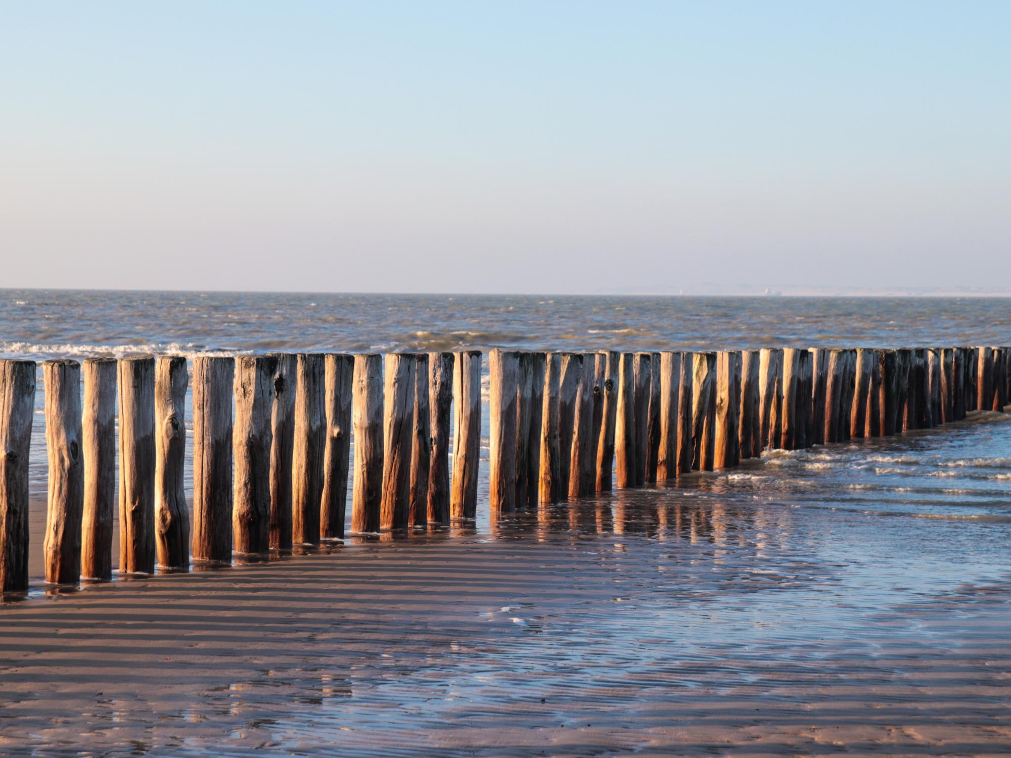 Blick vom Strand auf das Meer über eine Reihe Strandpfähle hinweg